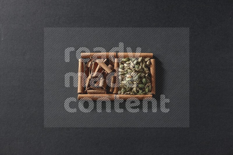 مربعان من أعواد القرفة ممتلئان بحبوب الهيل والقرفة علي خلفية سوداء