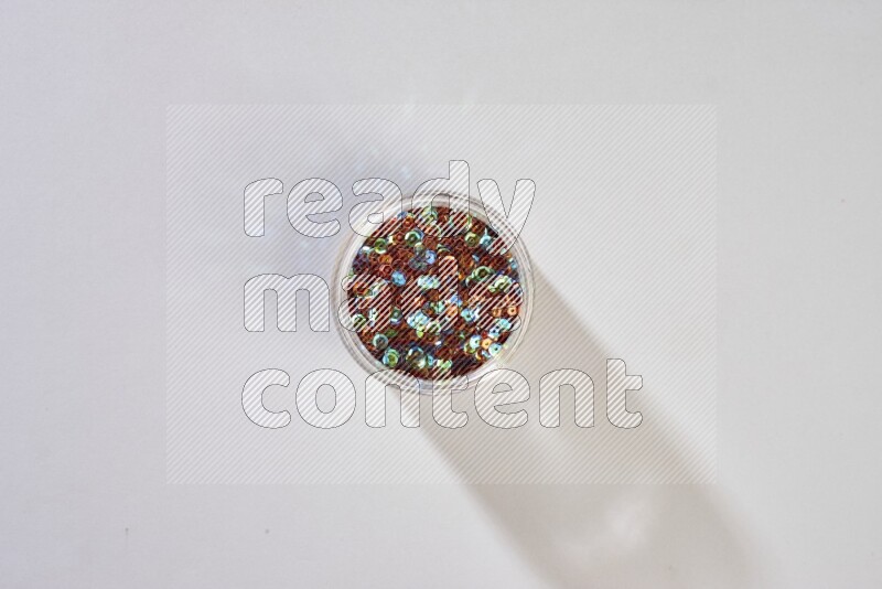 Colored flat sequins in a glass jar on grey background