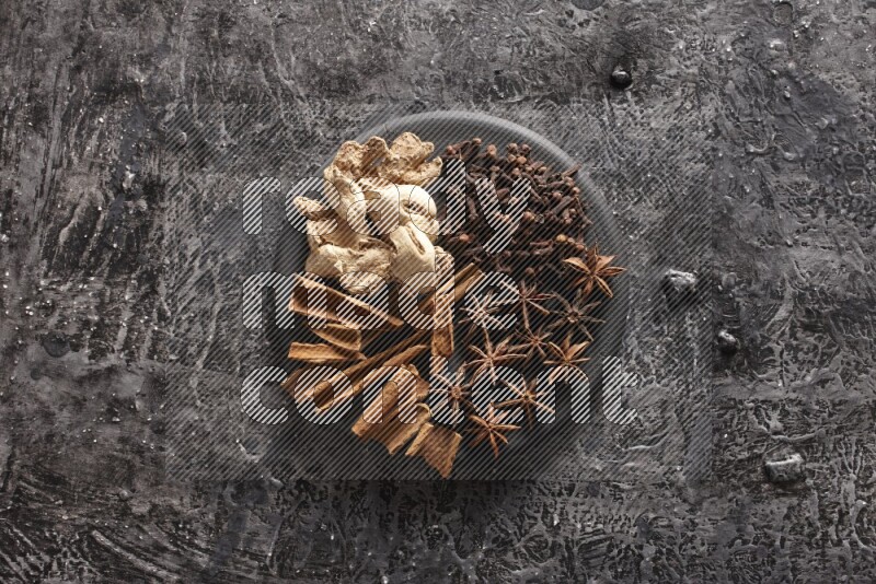 Ginger, cloves, star anise and cinnamon sticks on a black plate on textured black background