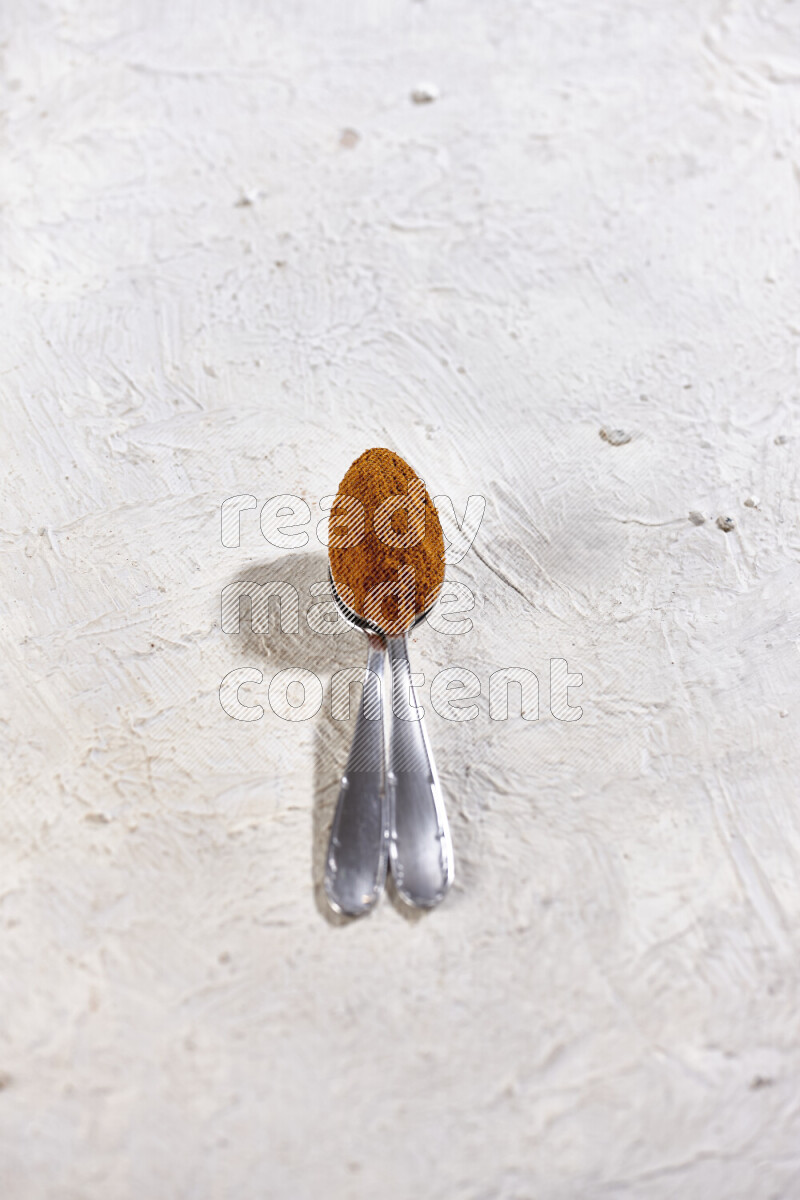 Two metal spoons full of ground paprika powder on white background