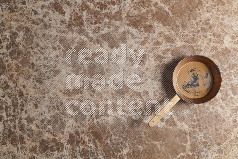 A small copper pan on beige marble background