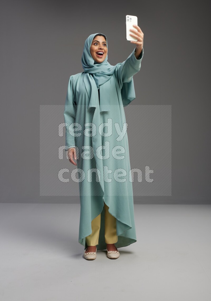 Saudi Woman wearing Abaya standing taking selfie on Gray background