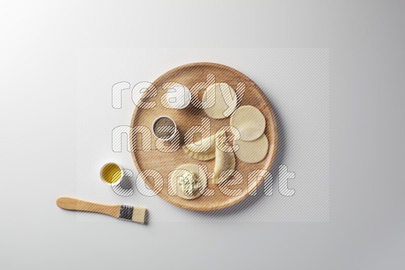 two closed sambosas and one open sambosa filled with cheese while salt, black pepper and oil with oil brush aside in a wooden dish on a white background