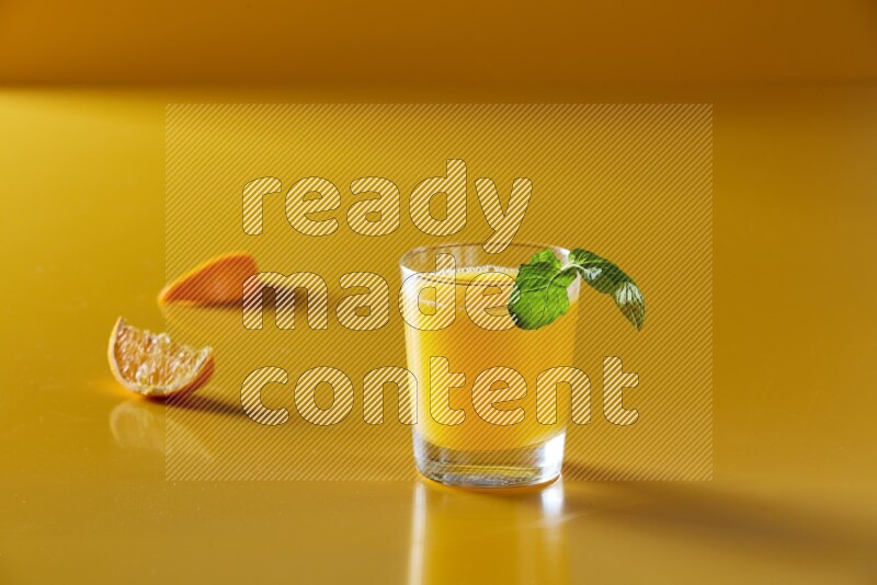 glass of orange juice with  mint on yellow background