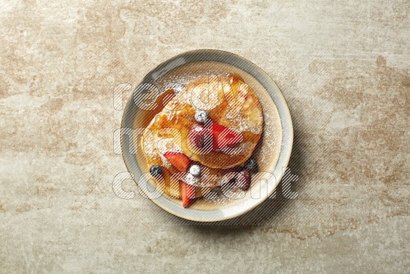Three stacked mixed berries pancakes in a bicolor plate on beige background
