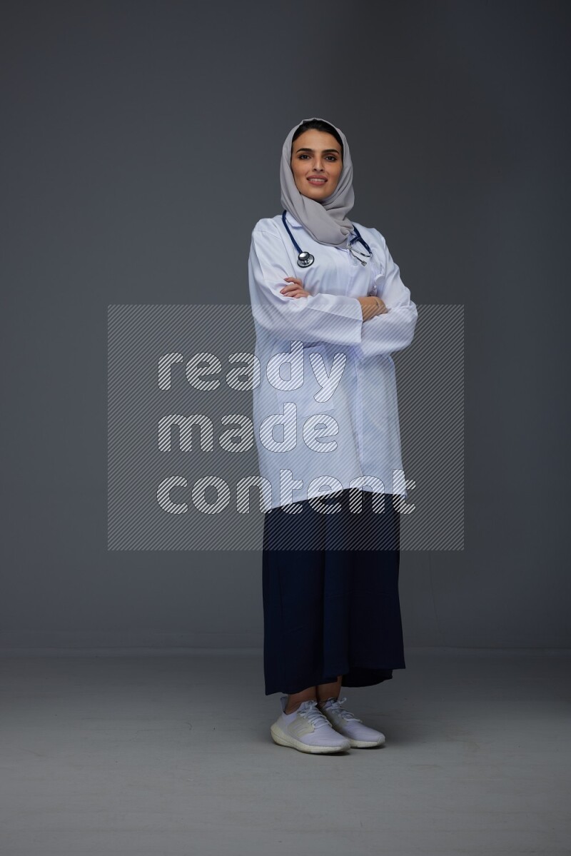 A female doctor wearing a light gray head scarf standing on grey background.