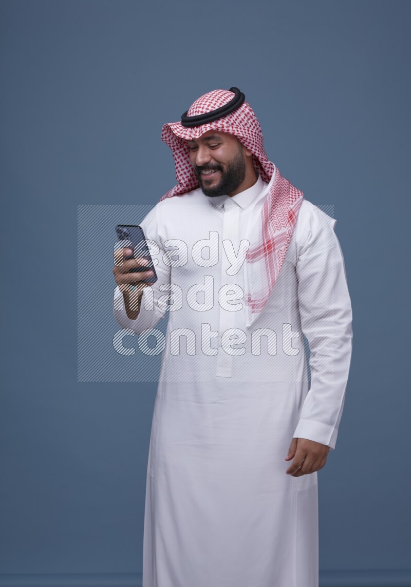 A man Texting on Blue Background wearing Saudi Thob and Shomag