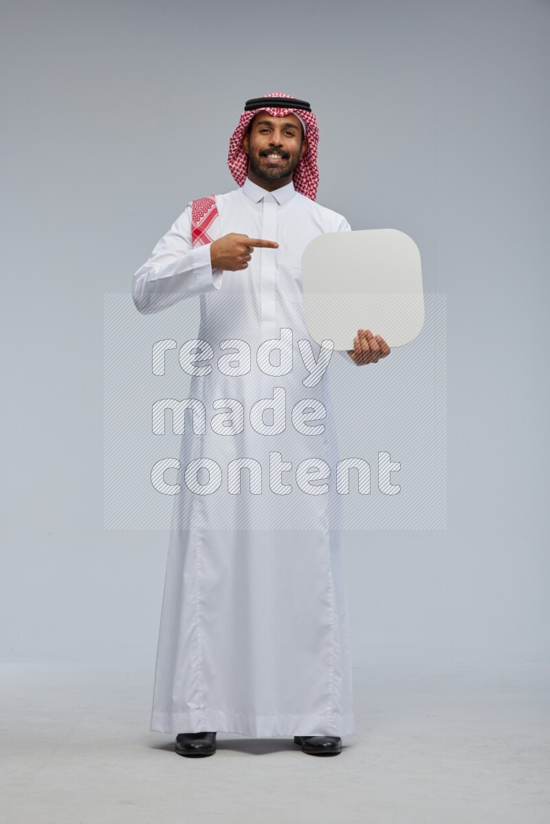 Saudi man Wearing Thob and shomag standing holding social media sign on Gray background