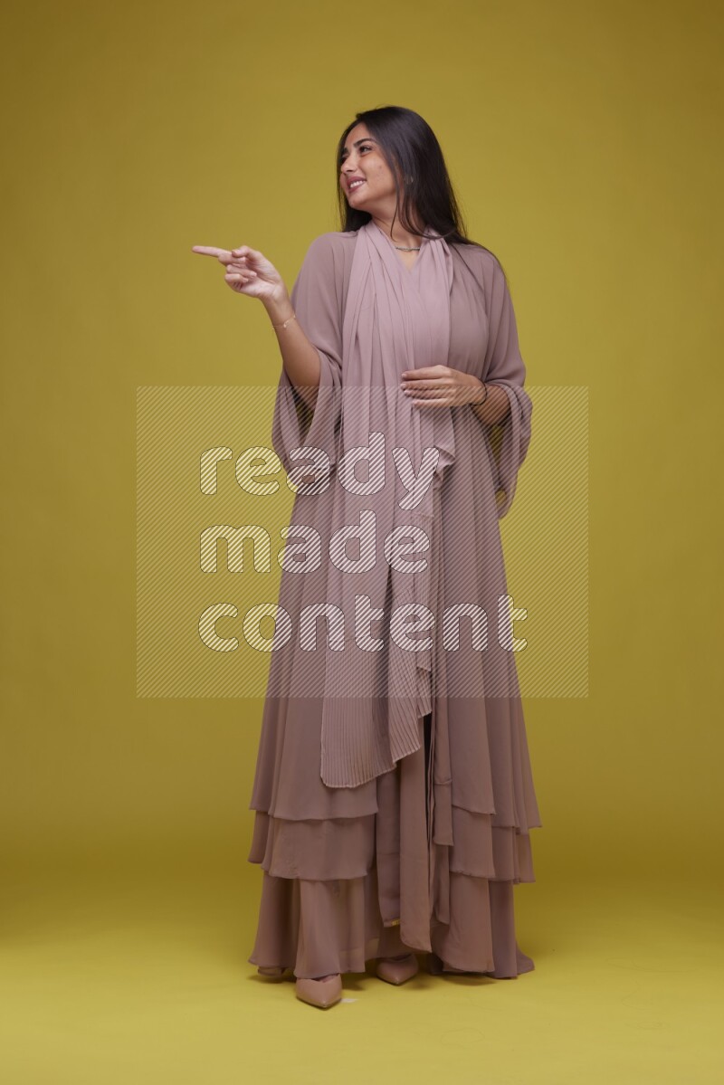 A woman Pointing on a Yellow Background wearing Brown Abaya
