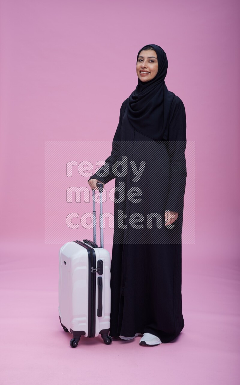 Saudi woman wearing Abaya standing holding bag on pink background