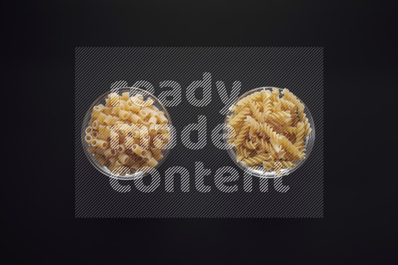 Different pasta types in glass bowls on black background