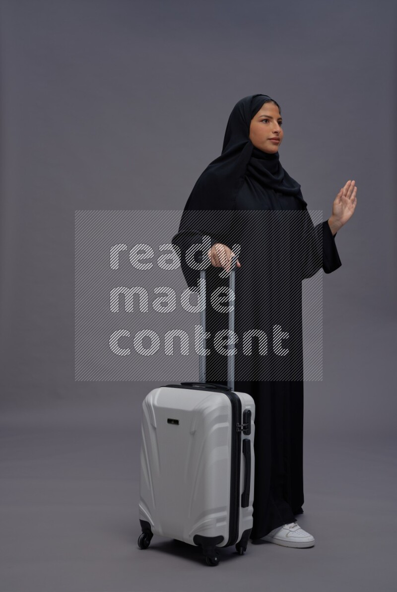 Saudi woman wearing Abaya standing holding bag on gray background