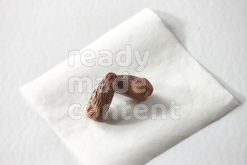 Two dried dates on a piece of paper on a white background in different angles