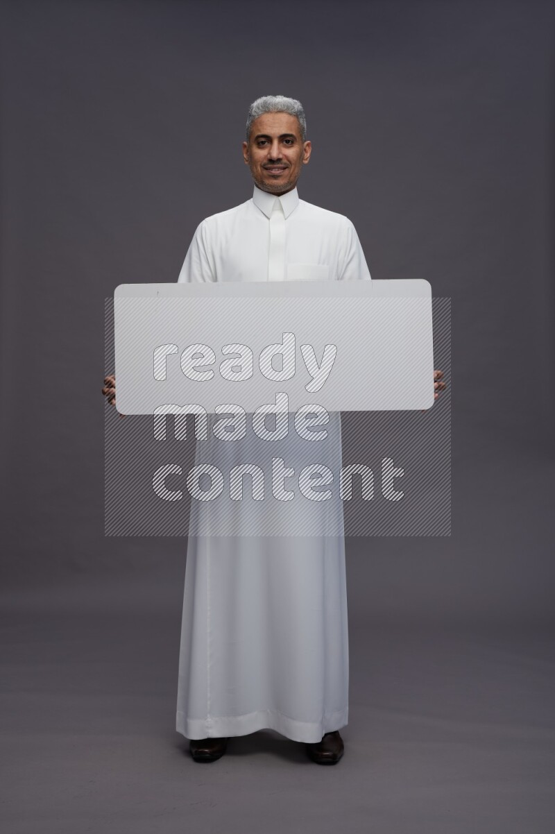 Saudi man wearing thob standing holding board on gray background