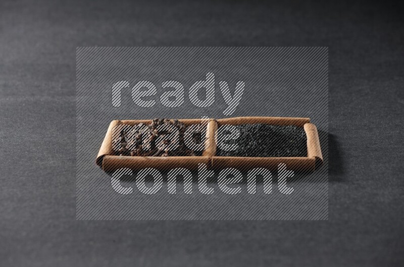 2 squares of cinnamon sticks full of black seeds and cloves on black flooring
