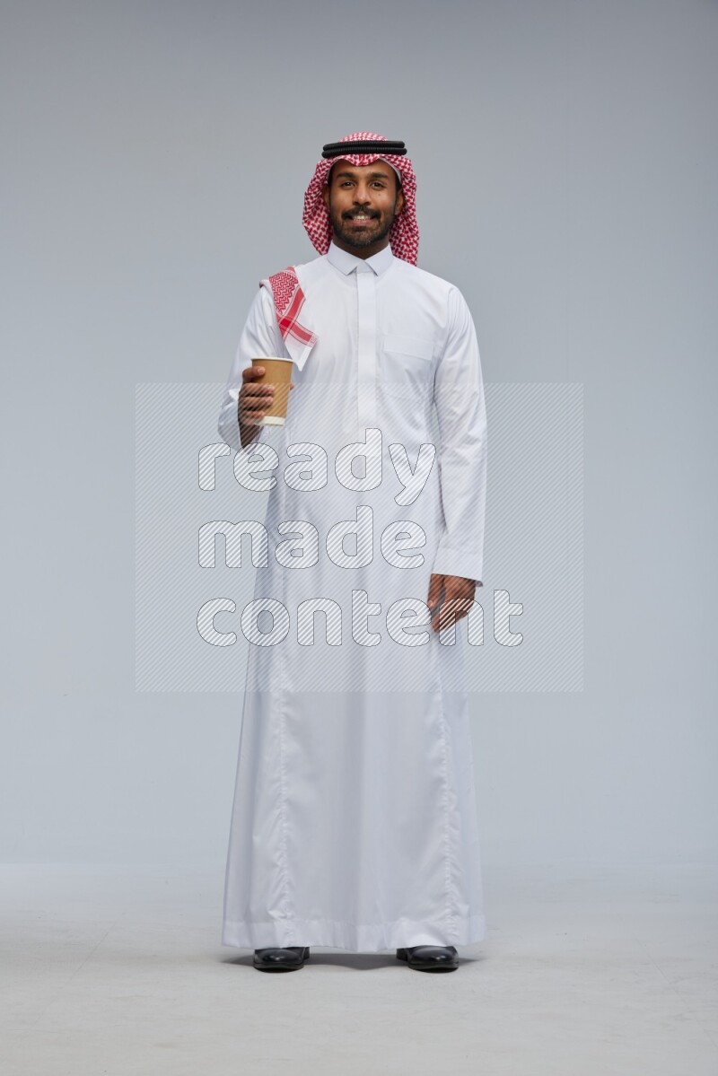 Saudi man Wearing Thob and shomag standing holding paper cup on Gray background