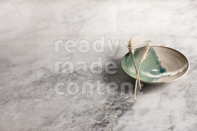 Wheat stalks on multicolored pottery plate on grey marble background