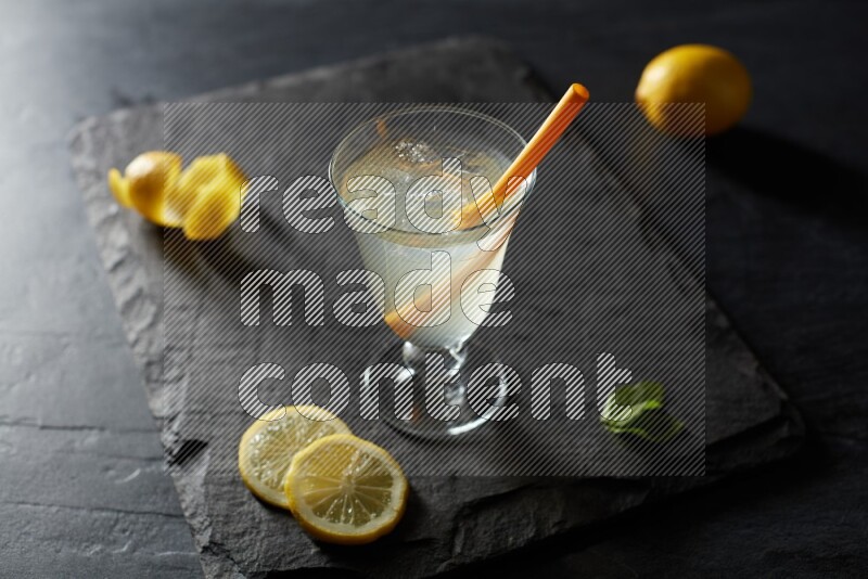 A glass of lemon juice with a straw on black background