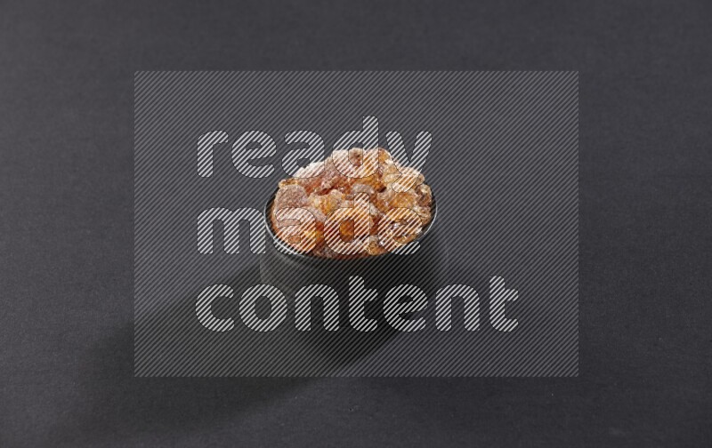 A black pottery bowl full of gum arabic on black flooring