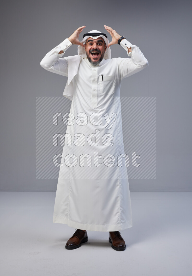 Saudi man Wearing Thob and white Shomag standing interacting with the camera on Gray background