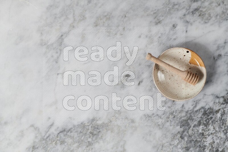 Multicolored pottery plate with wooden honey dipper in it on grey marble background