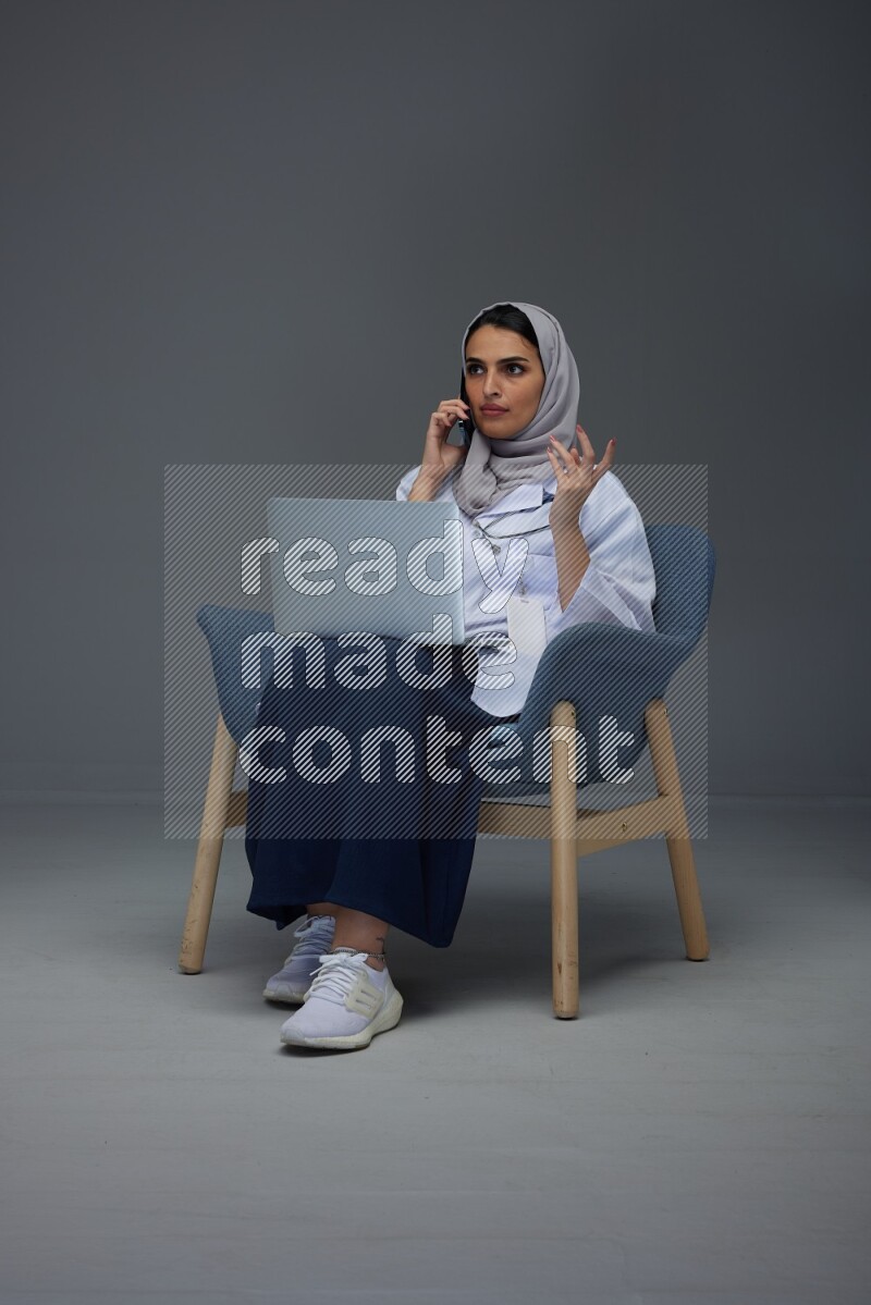 A doctor wearing a light gray head scarf sitting on blue chair on grey background