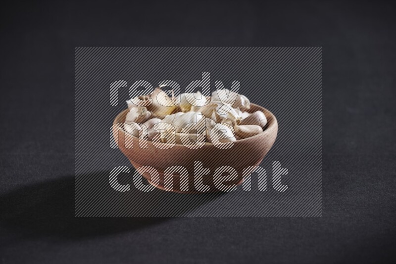 A wooden bowl full of garlic cloves on a black flooring