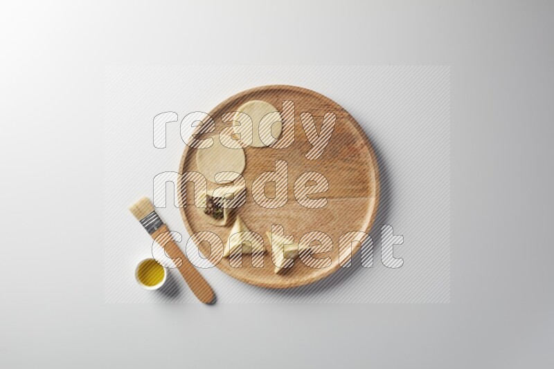 two closed sambosas and one open sambosa filled with meat while oil with oil brush aside in a wooden dish on a white background