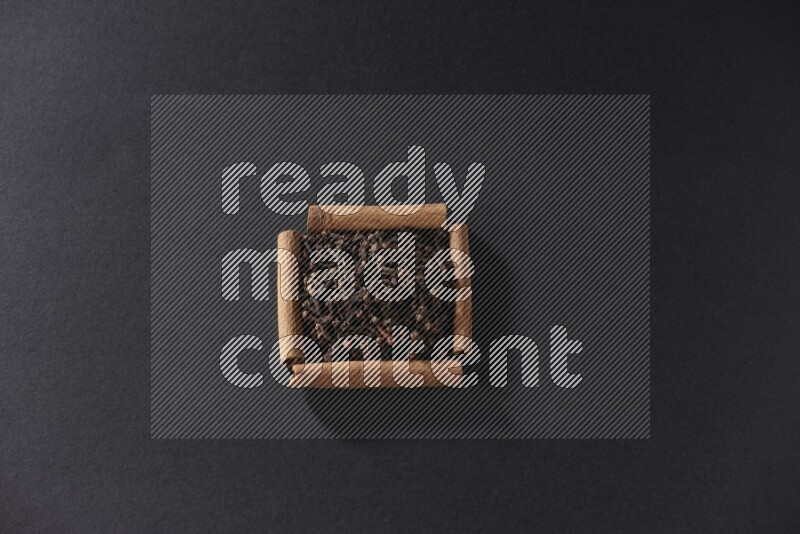 أربعة من أعواد القرفة مكونة شكل مربع بداخلها حبوب قرنفل علي خلفية سوداء