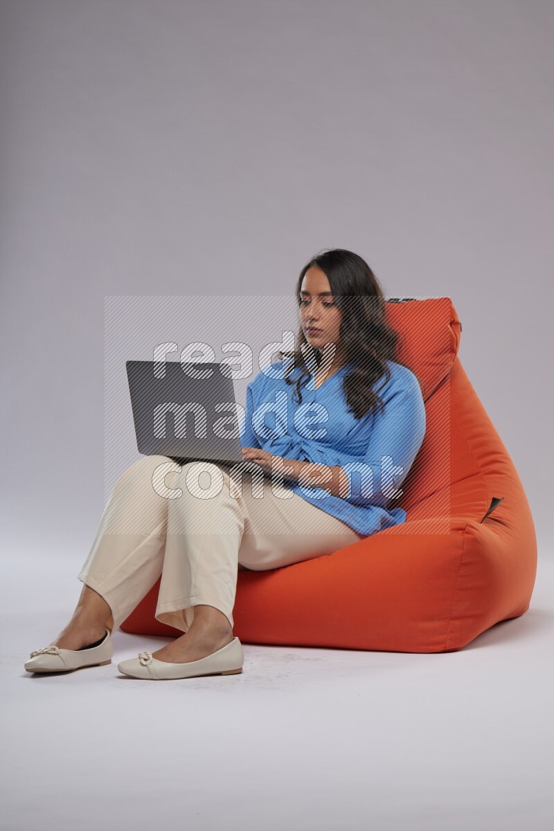 A woman sitting on an orange beanbag and working on laptop