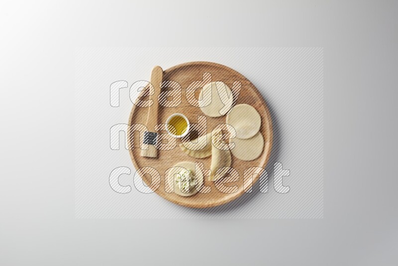 two closed sambosas and one open sambosa filled with cheese while oil with oil brush aside in a wooden dish on a white background