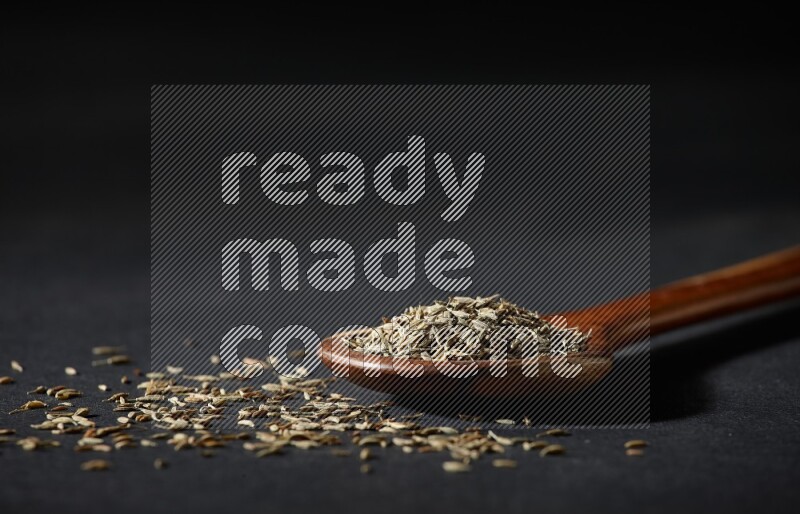 A wooden ladle full of cumin seeds on black flooring