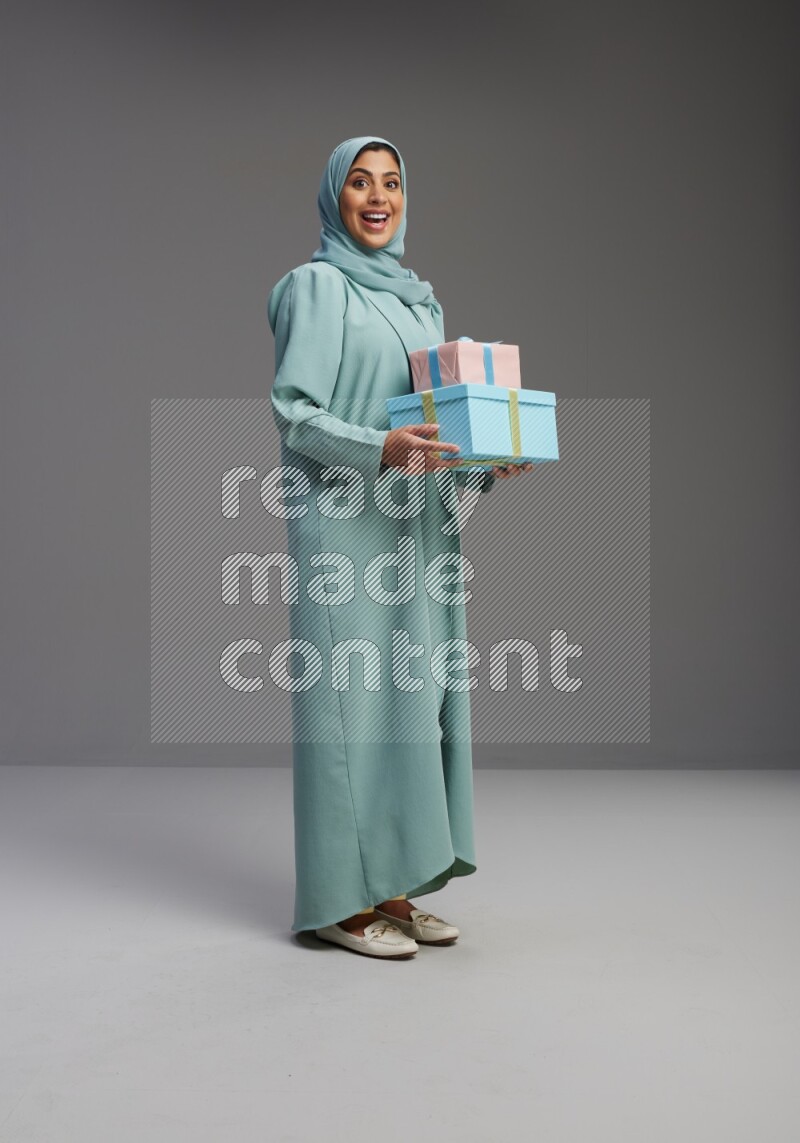 Saudi Woman wearing Abaya standing holding gift box on Gray background