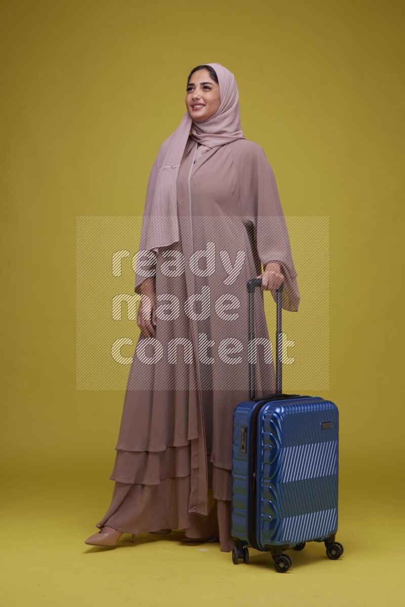 A woman With suit Case on a Yellow Background wearing Brown Abaya with Hijab
