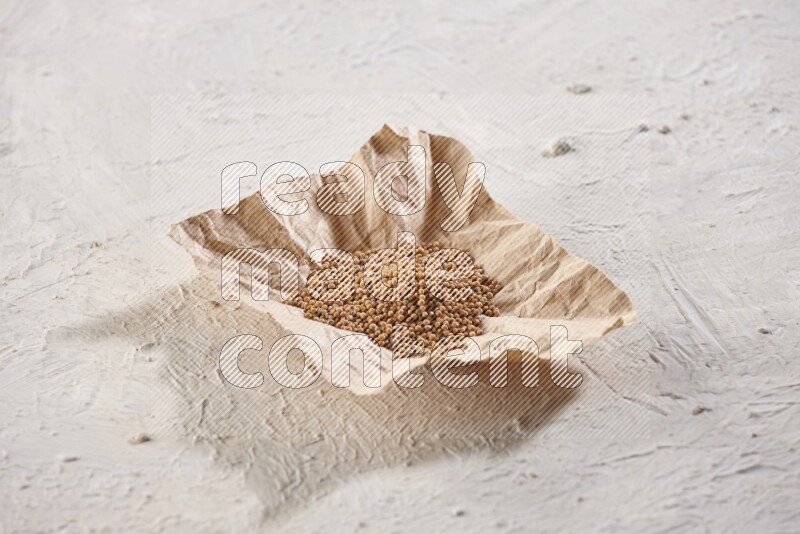 A crumpled piece of paper full of mustard seeds on a textured white flooring