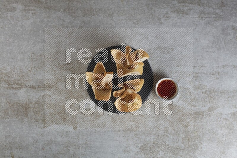 wonton cups with soy sauce ramkin on circle slate on grey textured counter top