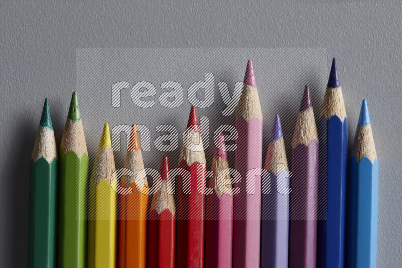 A collection of colored pencils arranged showcasing a gradient of different hues on grey background
