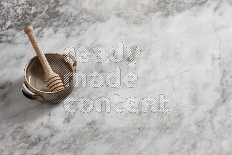 Multicolored pottery bowl with wooden honey dipper in it on grey marble background