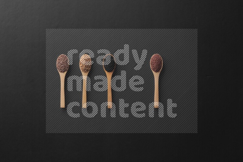 wooden spoons filled with white peppers, mustard seeds, black seeds, garden cress, cumin and flax on black flooring