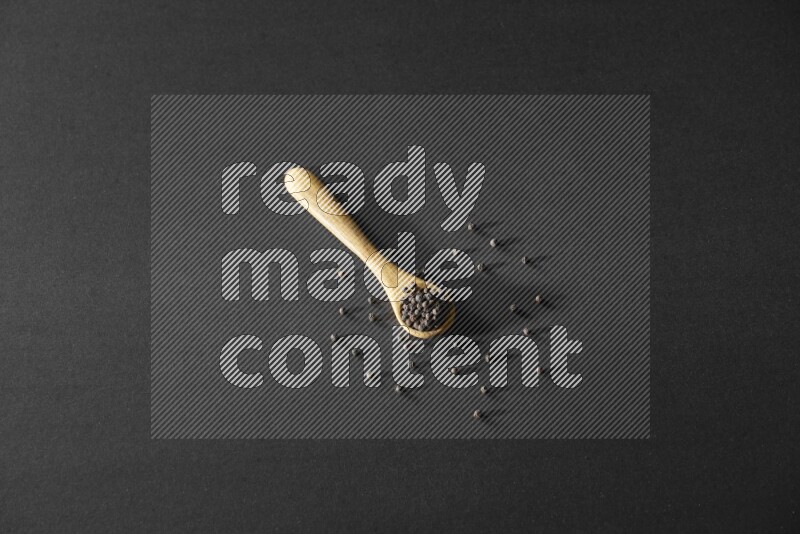 A wooden spoon full of black pepper on a black flooring