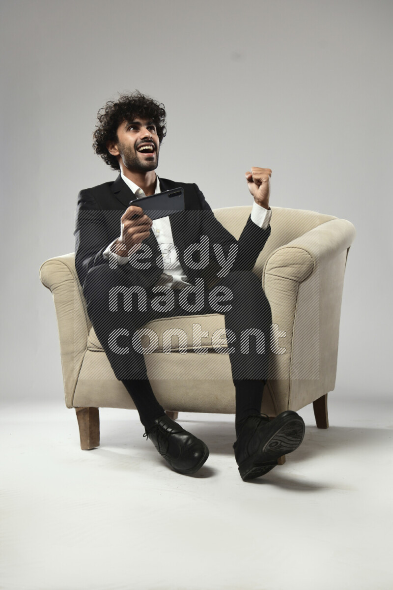 A man wearing formal sitting on a chair gaming on the phone on white background