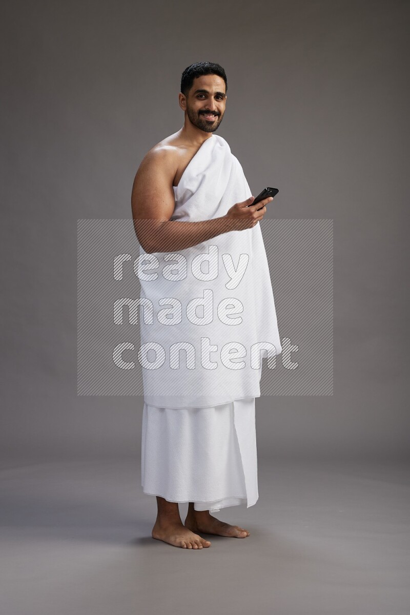 A man wearing Ehram Standing texting on phone on gray background