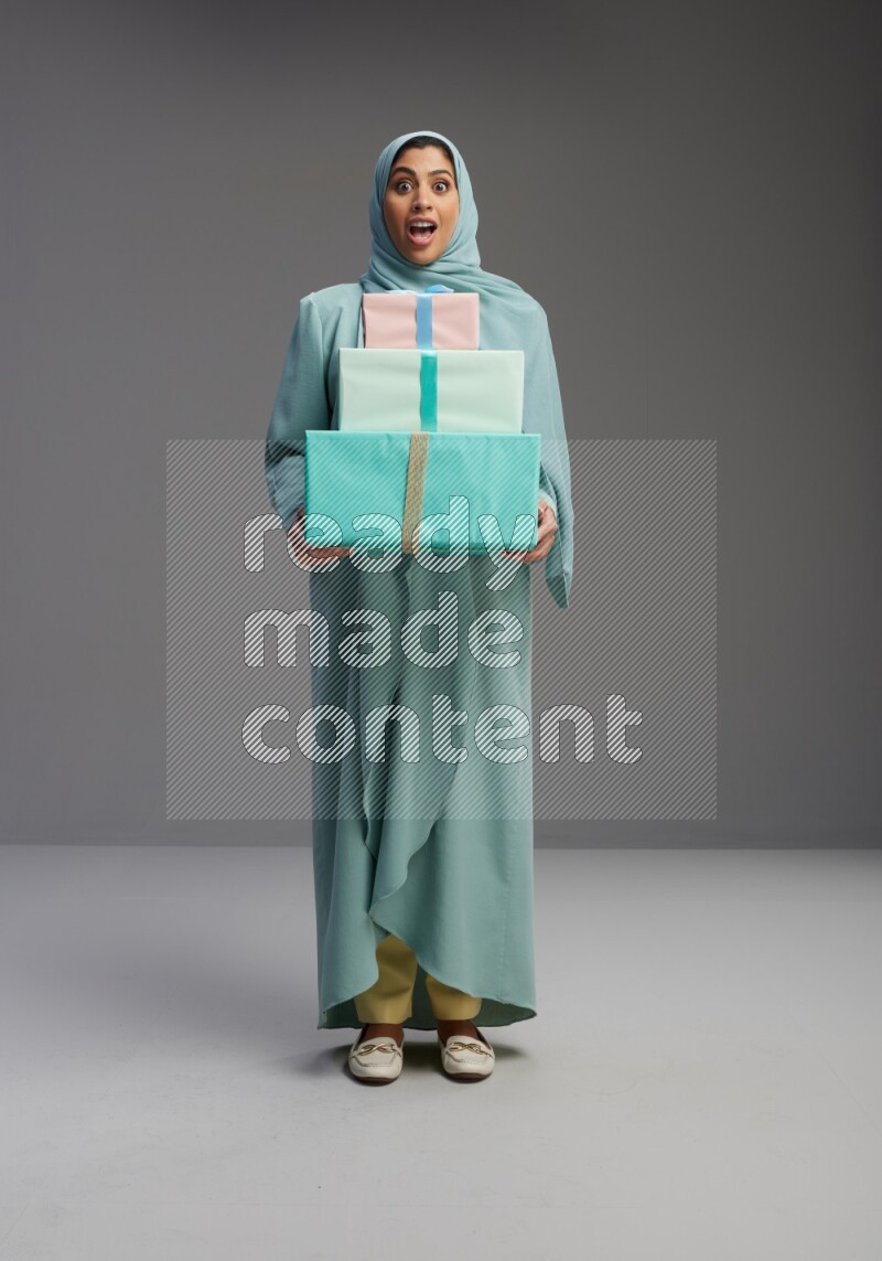 Saudi Woman wearing Abaya standing holding gift box on Gray background