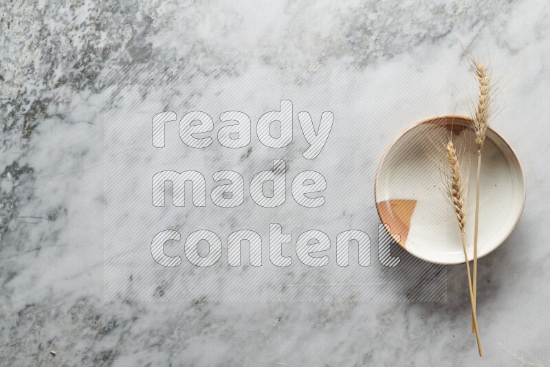 Wheat stalks on multicolored pottery plate on grey marble background