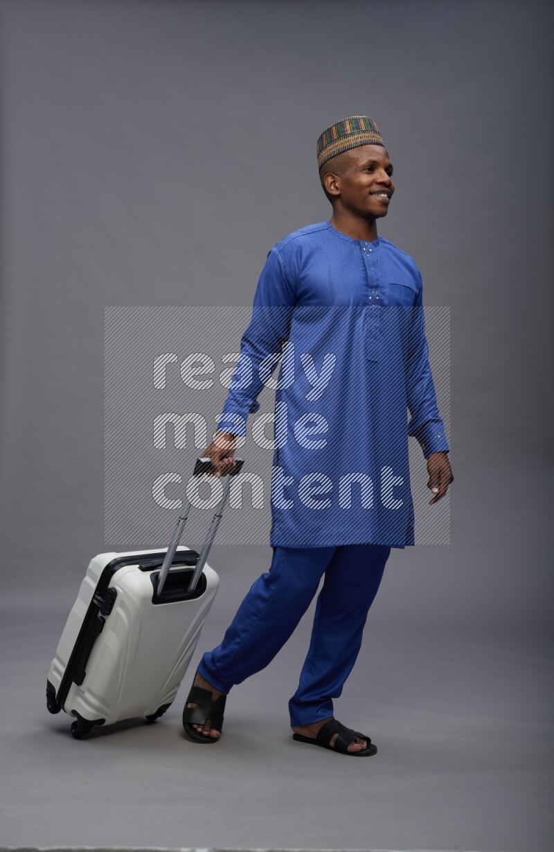Man wearing Nigerian outfit standing holding bag on gray background