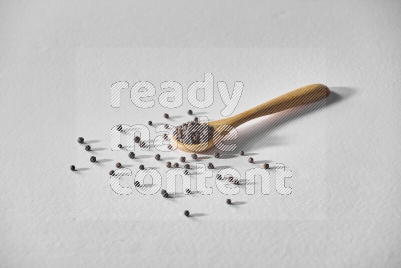 A wooden spoon full of black pepper on white flooring