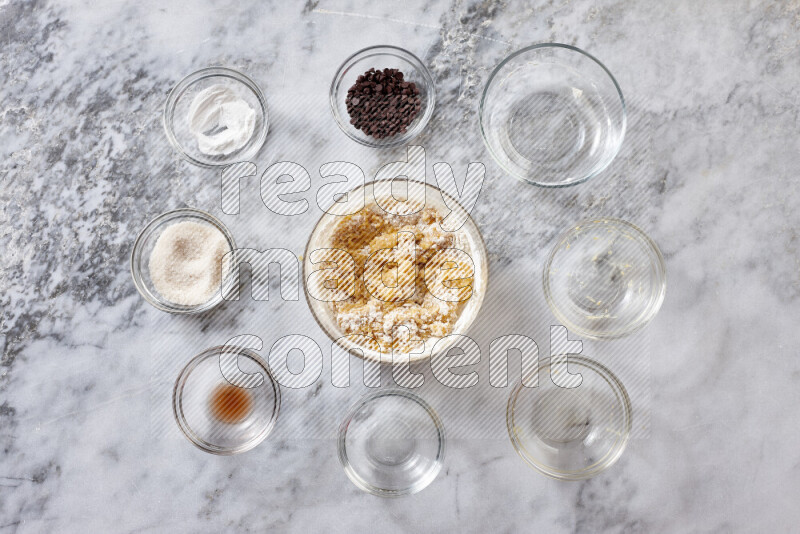 Cookies step by step with its ingredient, flour, butter, brown sugar, egg, vanilla extract, white sugar, chocolate chips and baking soda on grey marble background