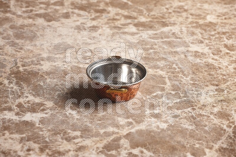 A small copper pot on beige marble background
