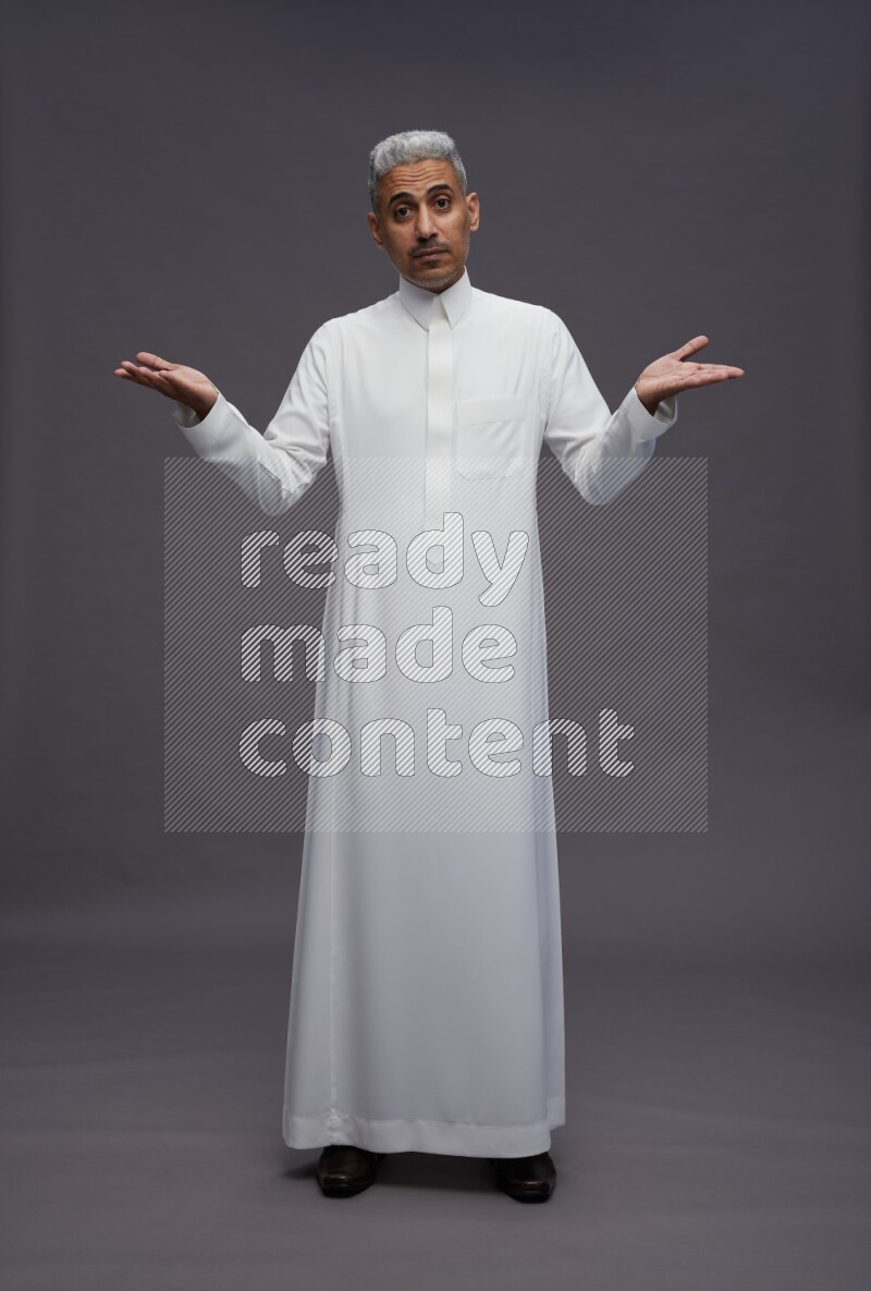 Saudi man wearing thob standing interacting with the camera on gray background
