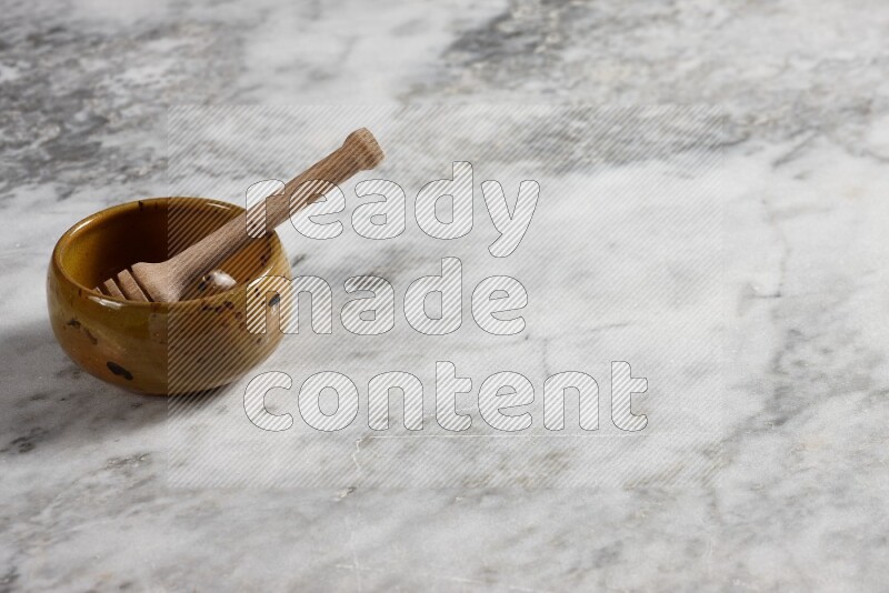 Multicolored pottery bowl with wooden honey dipper in it on grey marble background